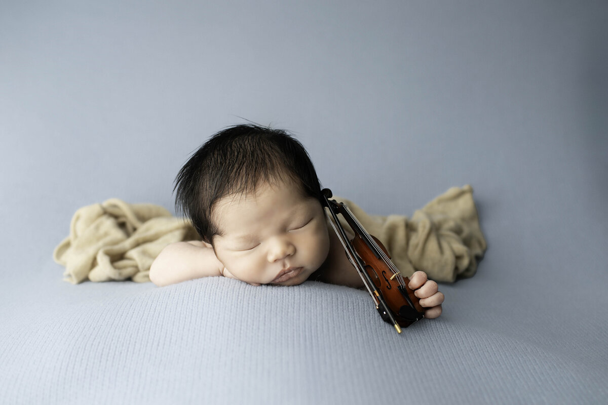 Newborn baby peacefully sleeping while gently holding a tiny violin, creating a charming and artistic scene with a delicate, musical touch