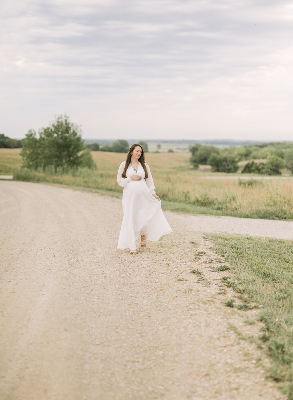 Pregnant woman walking confidently down a country dirt road with wide open sky and prairie in the background.