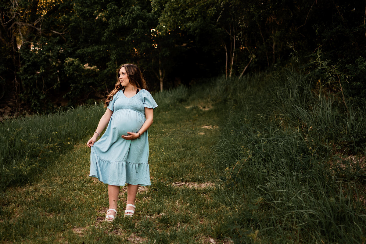 An expectant mother sways back and forth in her dress while looking to her right.