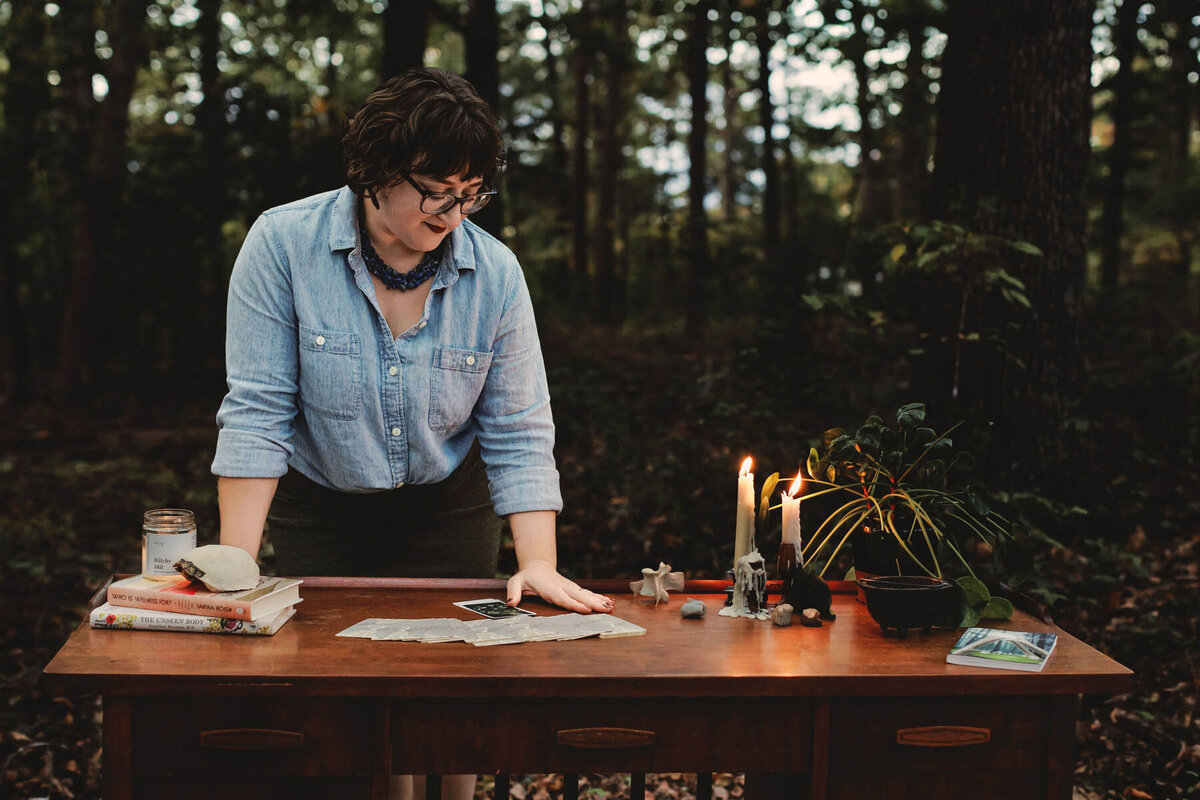 Energy worker Ash Stinson stands over a table in the forest where the Energy Archaeology Oracle Deck is spread out and a single card has been pulled for a reading