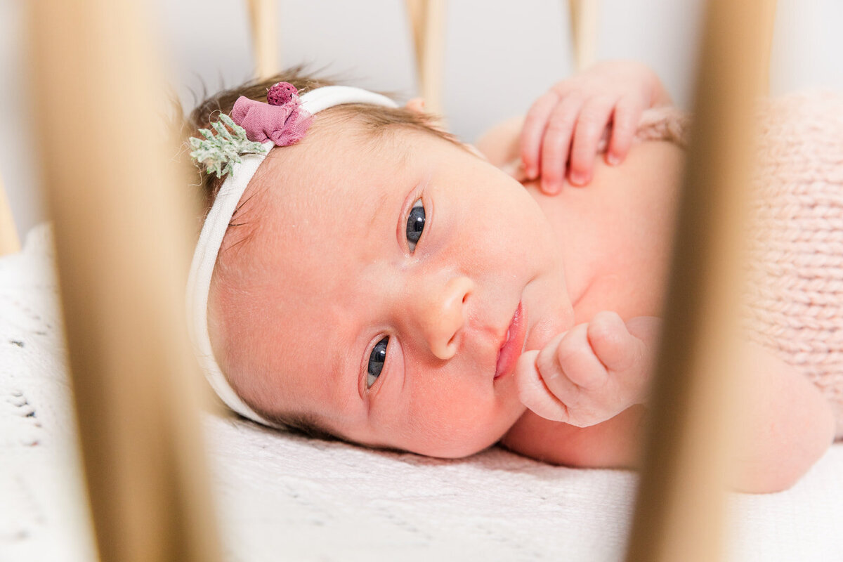 newborn baby girl looking trough crib side