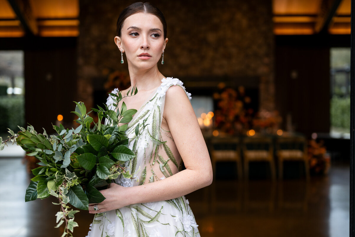 Elegant bride holding eucalyptus bouquet in flowing botanical print dress at Estate Yountville wedding venue, captured by San Francisco Bay Area wedding photographer