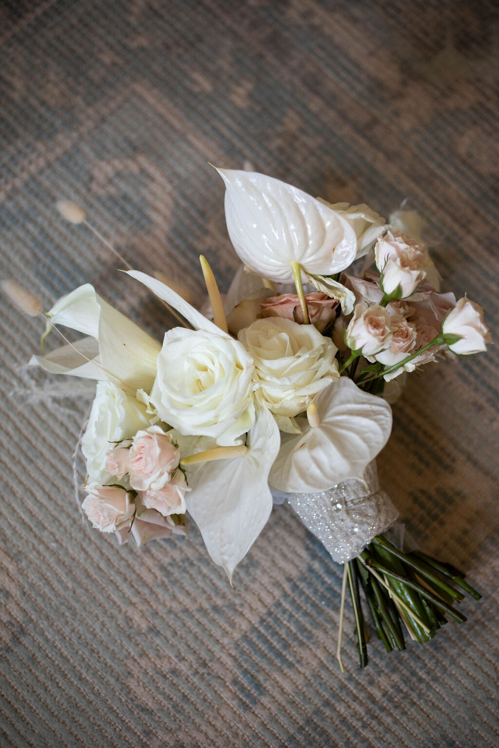 A stunning bridal bouquet with white roses, blush-toned florals, and elegant anthuriums wrapped in a crystal-studded ribbon.