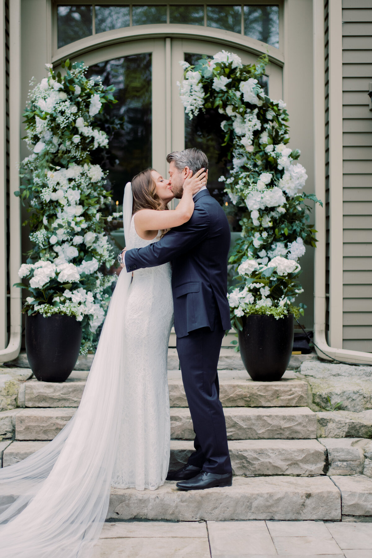 A bride and groom sharing a heartfelt first kiss in front of a beautiful floral arch during their ceremony