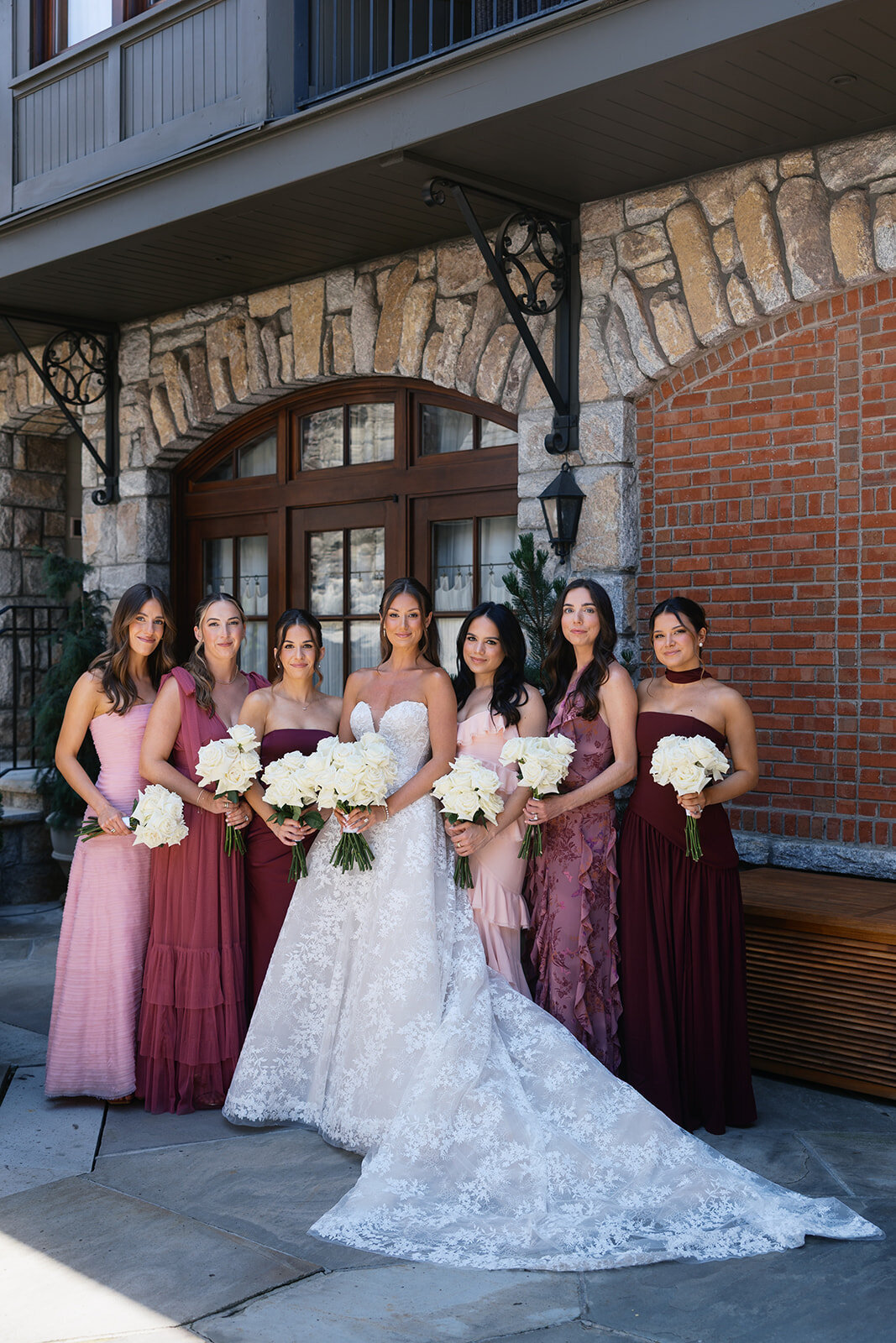 Elegant group bridesmaids portrait in pink and burgundy gowns with white rose bouquets outside Old Edwards Inn in Highlands, NC.
