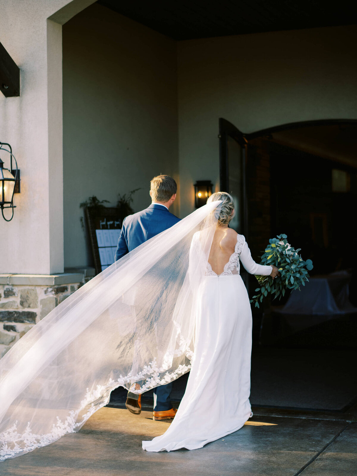 Bride with cathedral length veil walks with her husband into wedding reception at Canyonwood Ridge