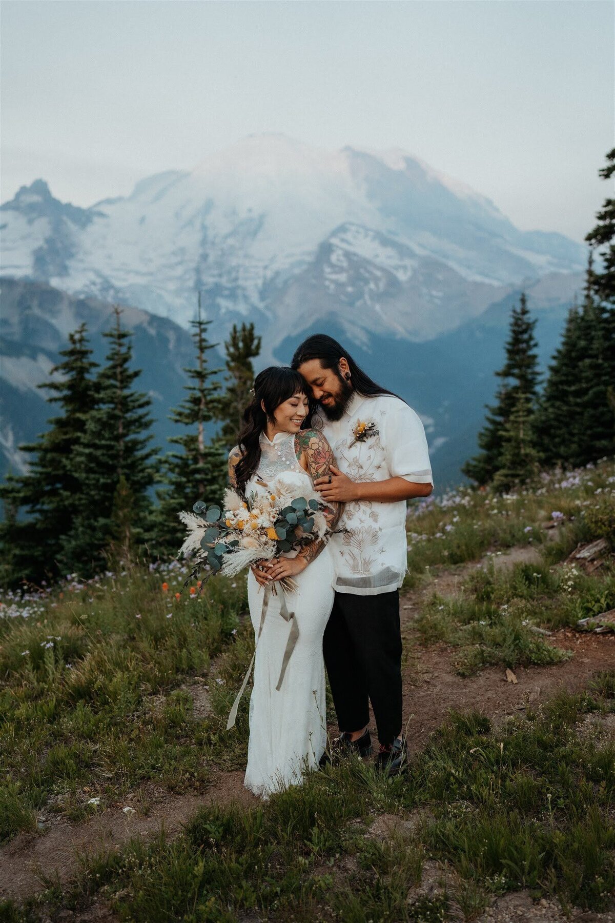 Bride with bouquet & groom snuggling up on a trail in front of Mount Rainier during their hiking elopement!