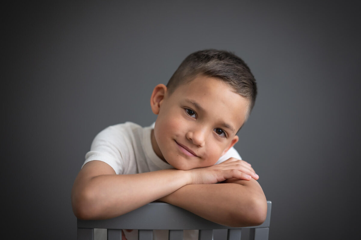 handsome 8 year old boy in studio portrait leaning arms on the back of a chair