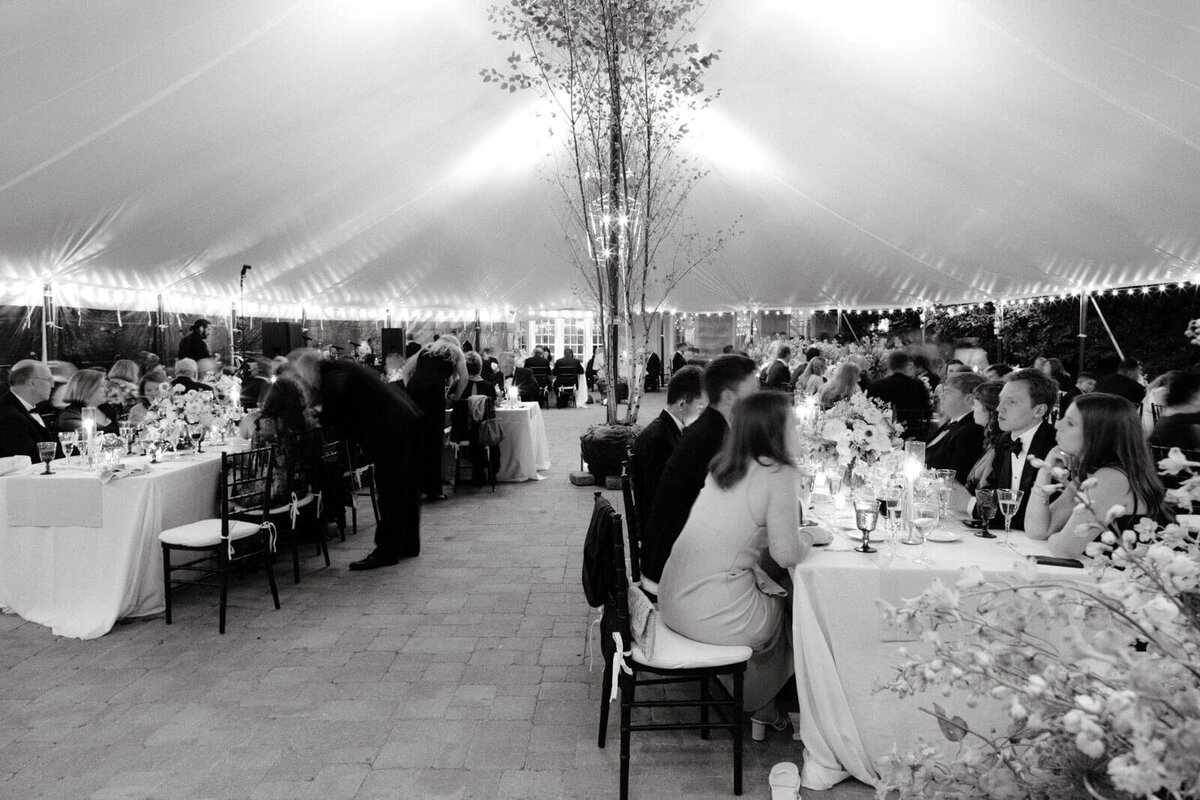The seated wedding guests are chatting in an elegant wedding tent reception at Lion Rock Farm, CT. Image by Jenny Fu Studio