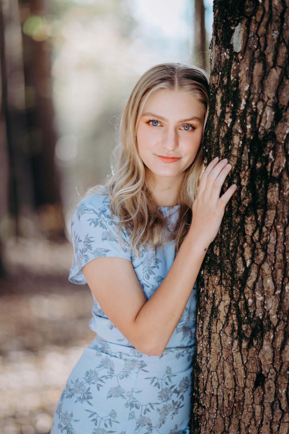 Beautiful portrait of a senior girl in a blue dress leaning against a tree.