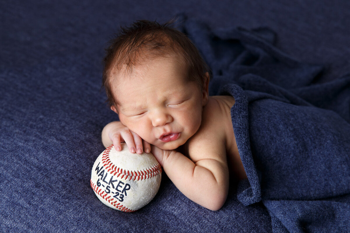 Newborn baby boy sleeping in blue blanet and resting on a baseball
