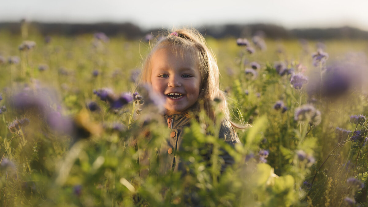 Mädchen steht lachend auf einer Blumenwiese
