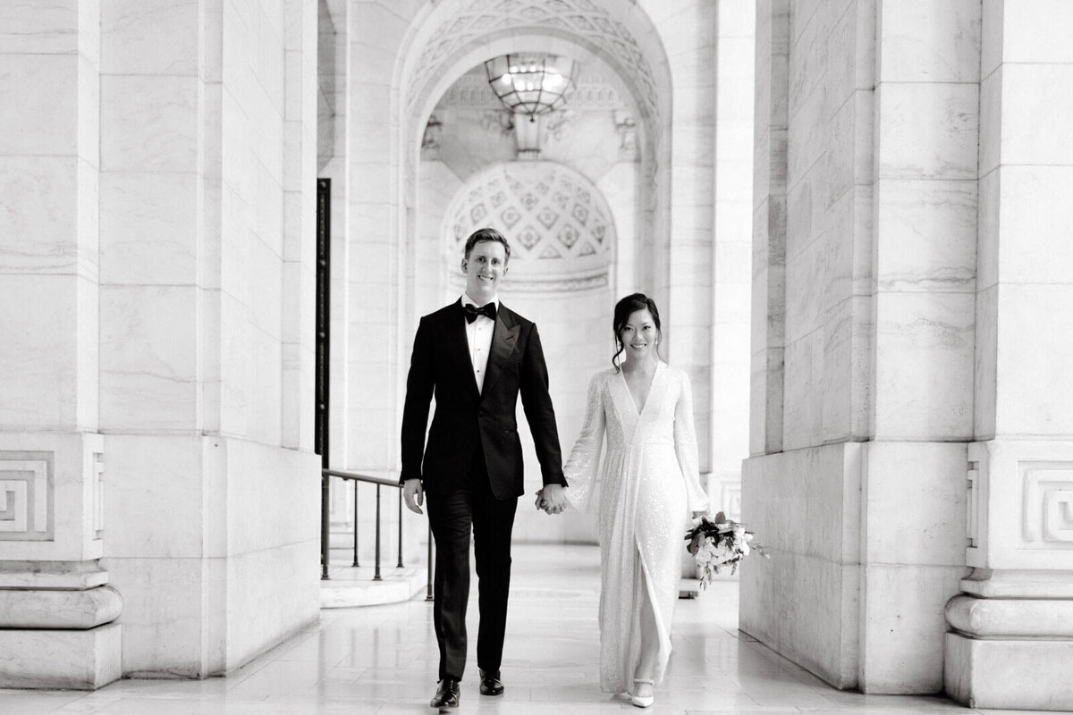 The bride and the groom are happily walking in the hallway of the New York Public Library, NYC. Image by Jenny Fu Studio