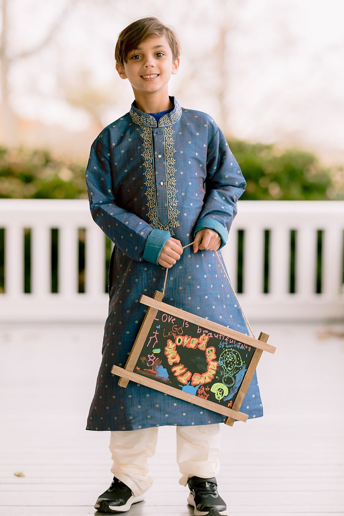 Indian ring bearer holding a chalkboard sign at Ravenswood Mansion wearing a blue and white sherwani.