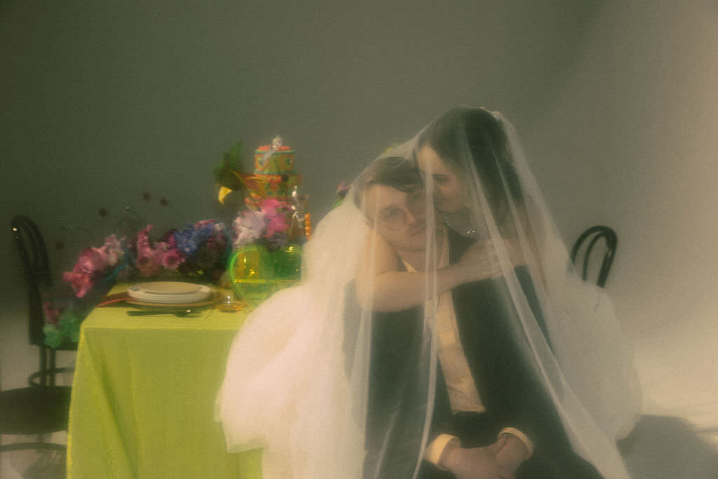 A wedding couple sitting behind each other with a veil over them.