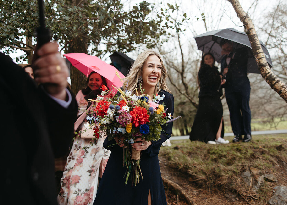 A woman laughing joyously, holding a vibrant bouquet under a pink umbrella