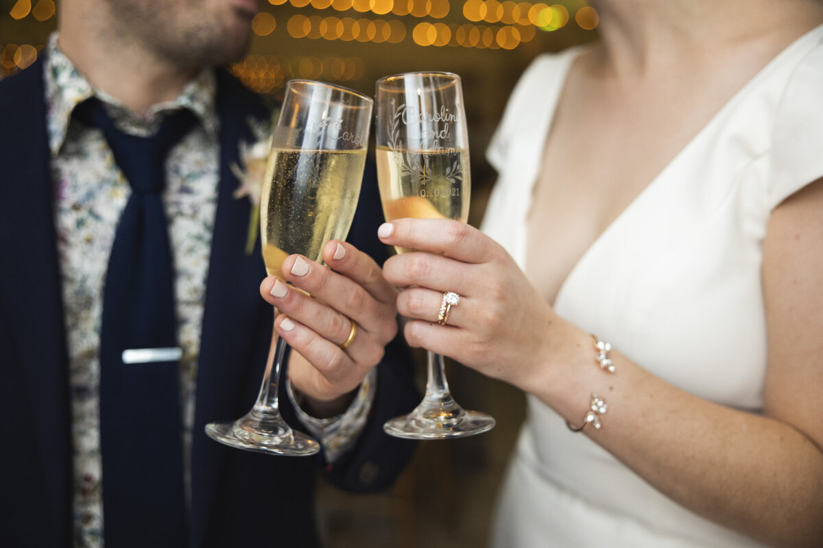 A close up of two people toasting with champagne and showing off their wedding rings 