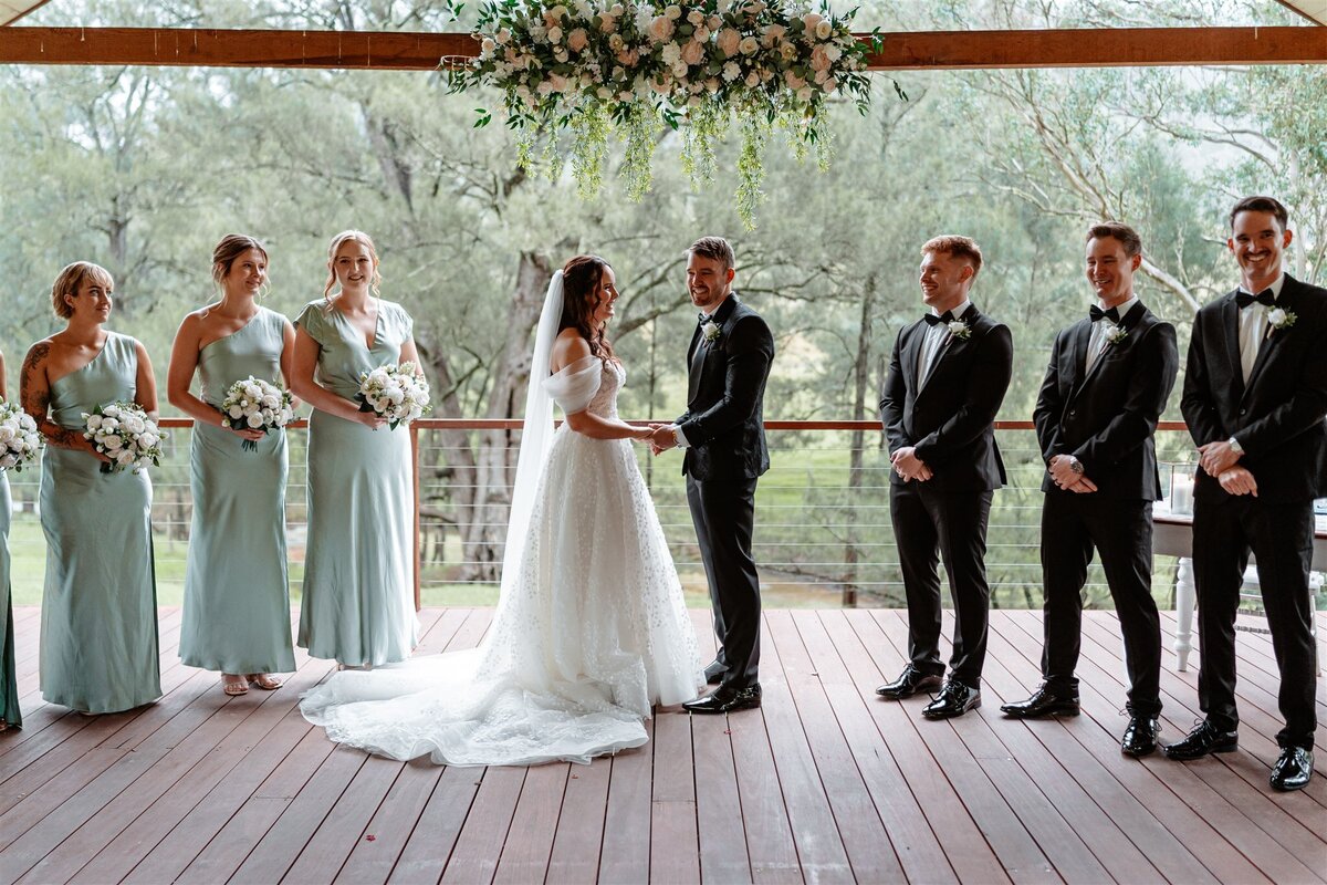 A radiant bride, adorned in ivory lace, exchanges vows with her beaming groom under a canopy of blooming roses at their enchanting garden ceremony.