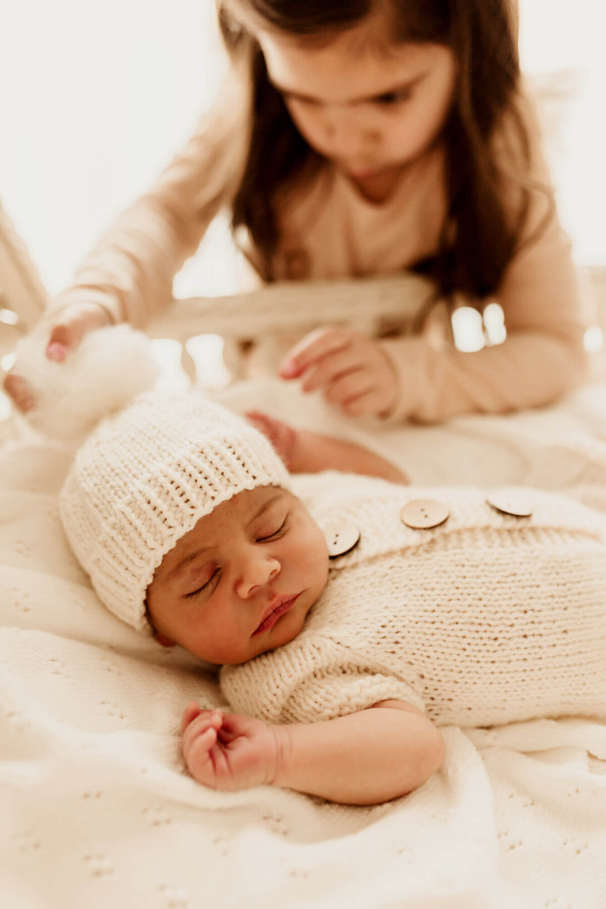 sister peers into a bassinet with her baby bother in it.