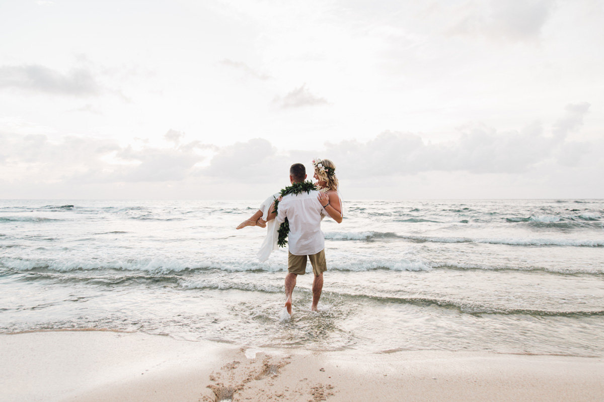 Groom carries bride into the ocean after they elope in Hawaii