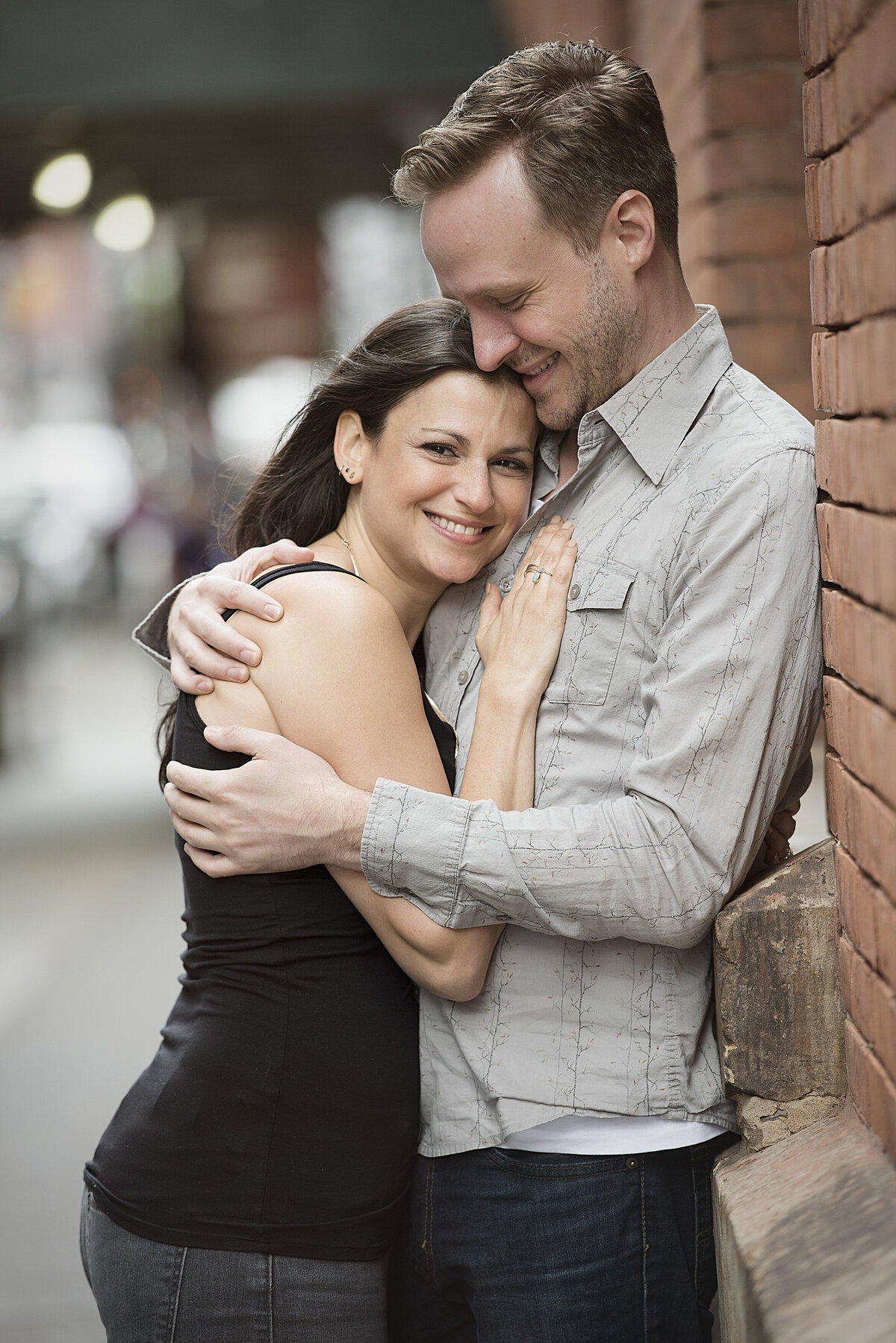 A couple hugging as they lean against a brownstone