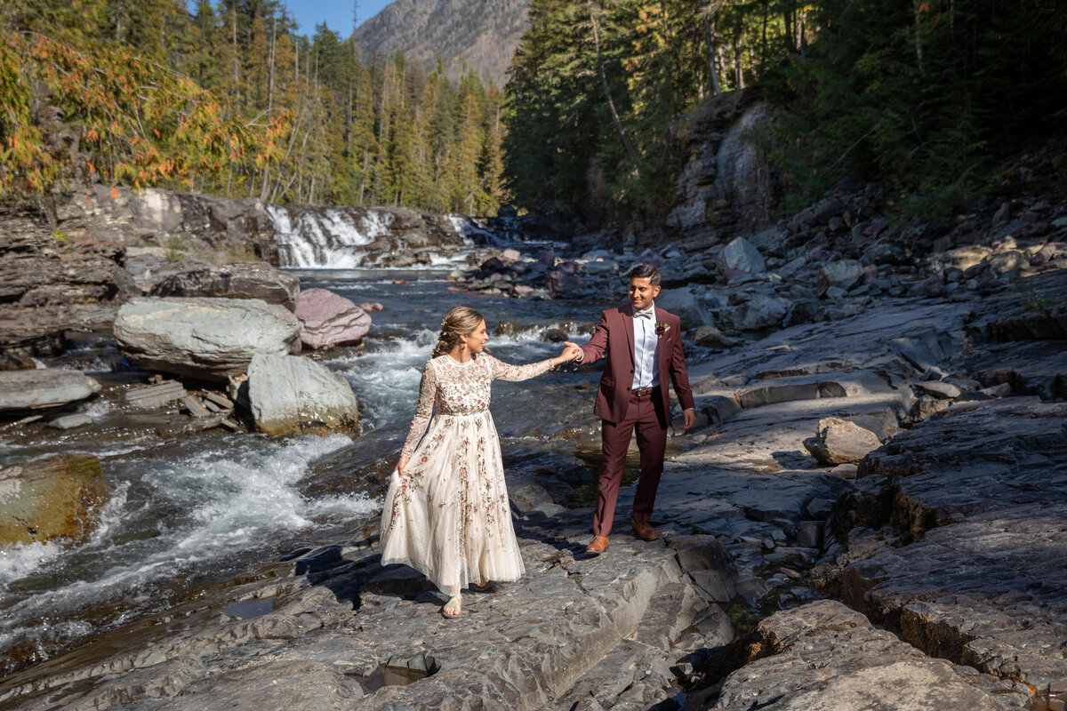 A bride walks in front of her groom looking back over her shoulder at him as their Montana elopement photographer take their picture.