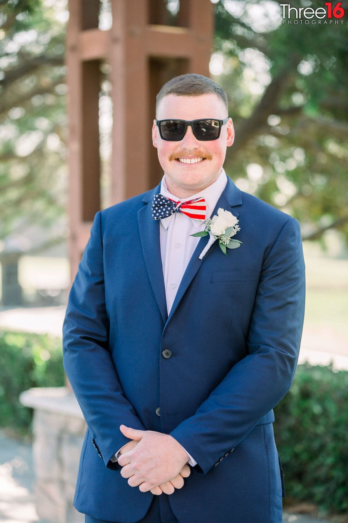 Groom poses with large smile, hands crossed and sunglasses on