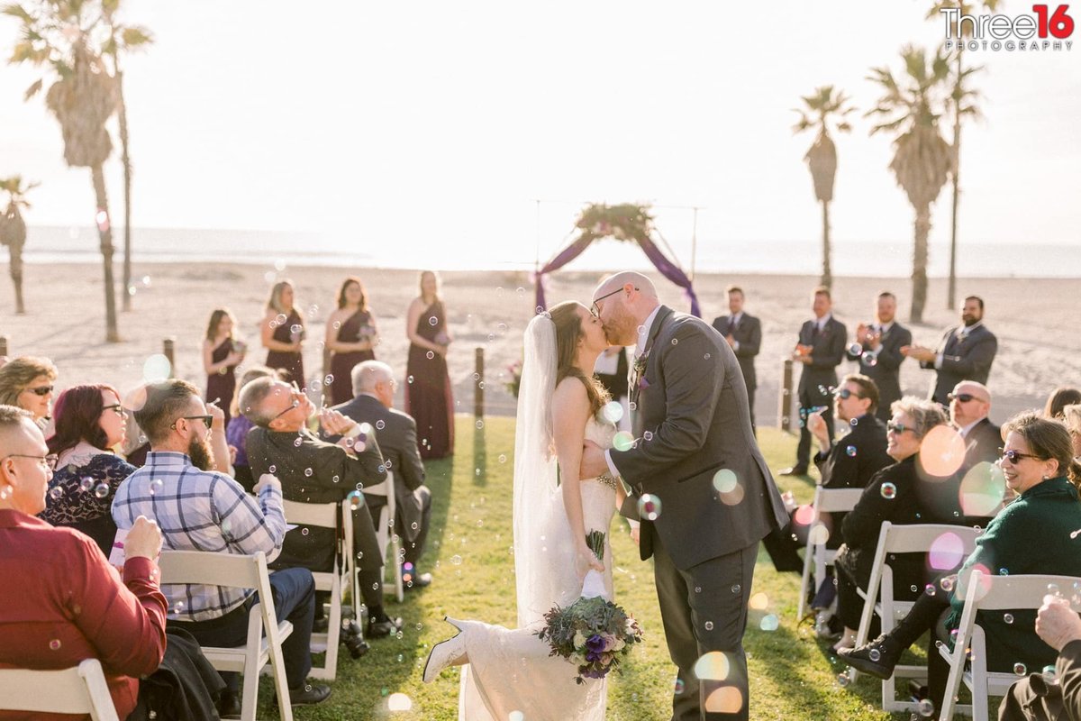 Bride and Groom share a kiss at the end of the aisle amongst all their wedding guests