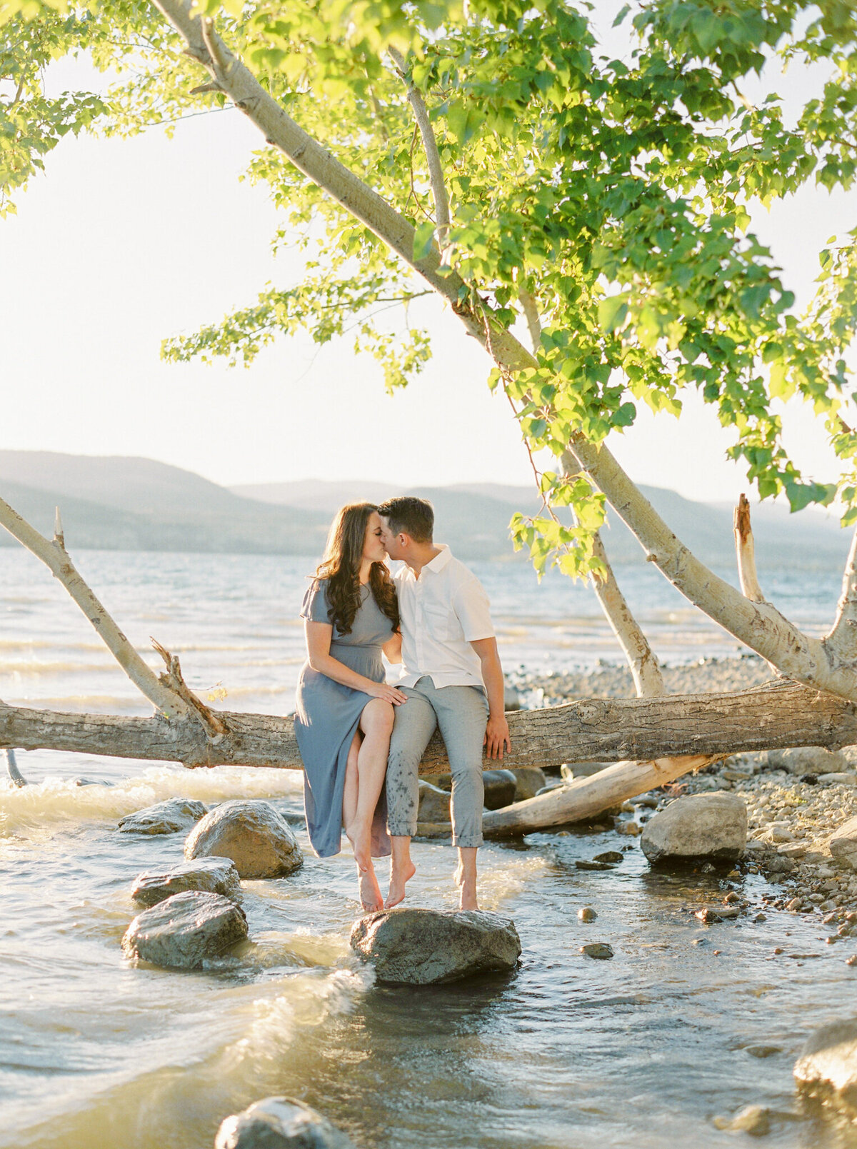 Beautiful engagement session inspiration, couple sitting on a tree branch over water, captured by Justine Milton Photography, fine art  wedding photographer & videographer in Calgary Alberta. Featured on the Bronte Bride Vendor Guide.