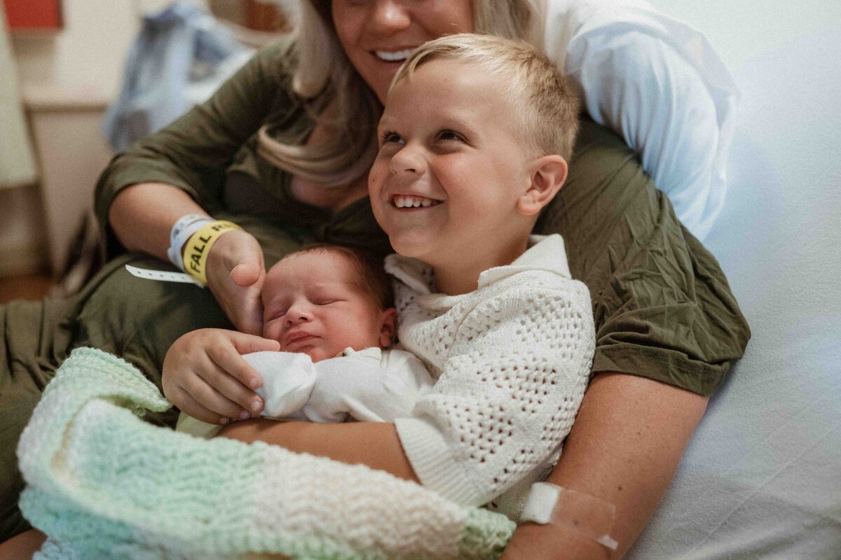 big brother smiling and holding his little brother while meeting him for the first time at the hospital after birth, documented by pa fresh 48 photographer kristin wieskamp
