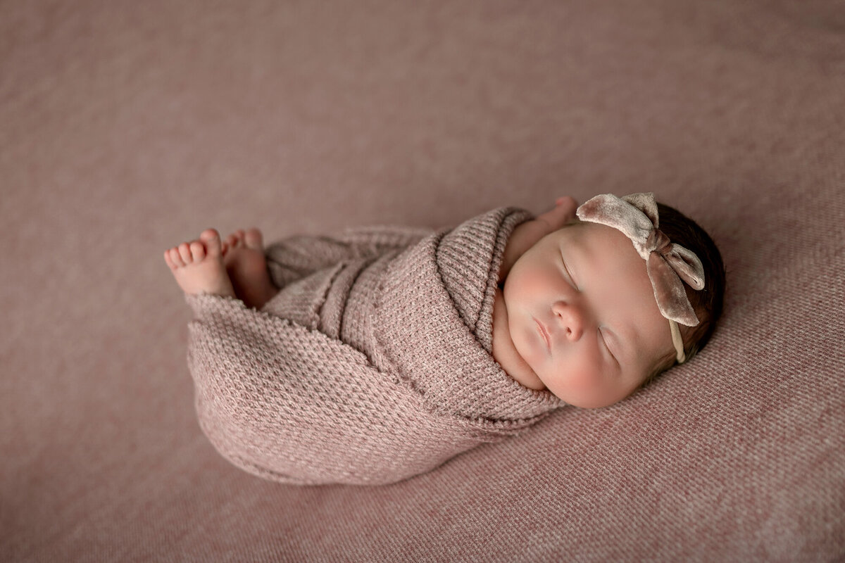 A sleeping newborn girl in a knit swaddle with matching headband