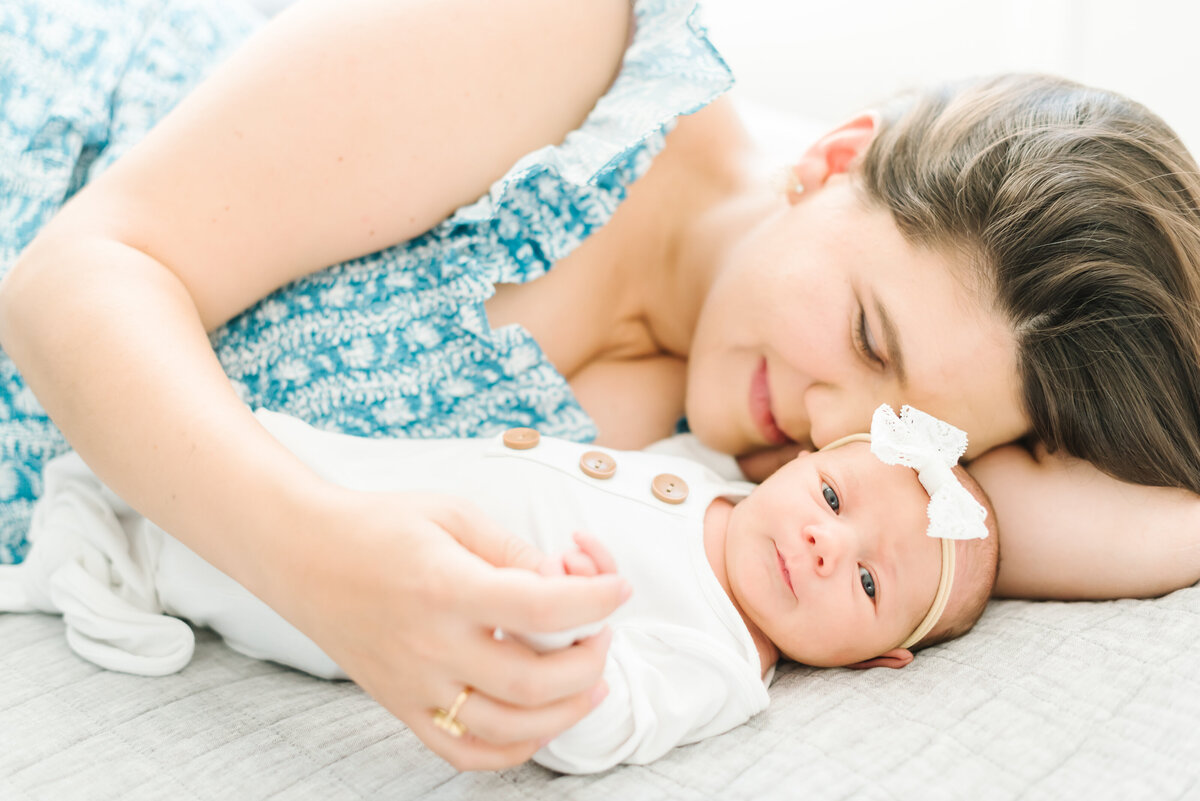 Mom in blue dress snuggling newborn baby in bow - Washington DC Newborn Photographer