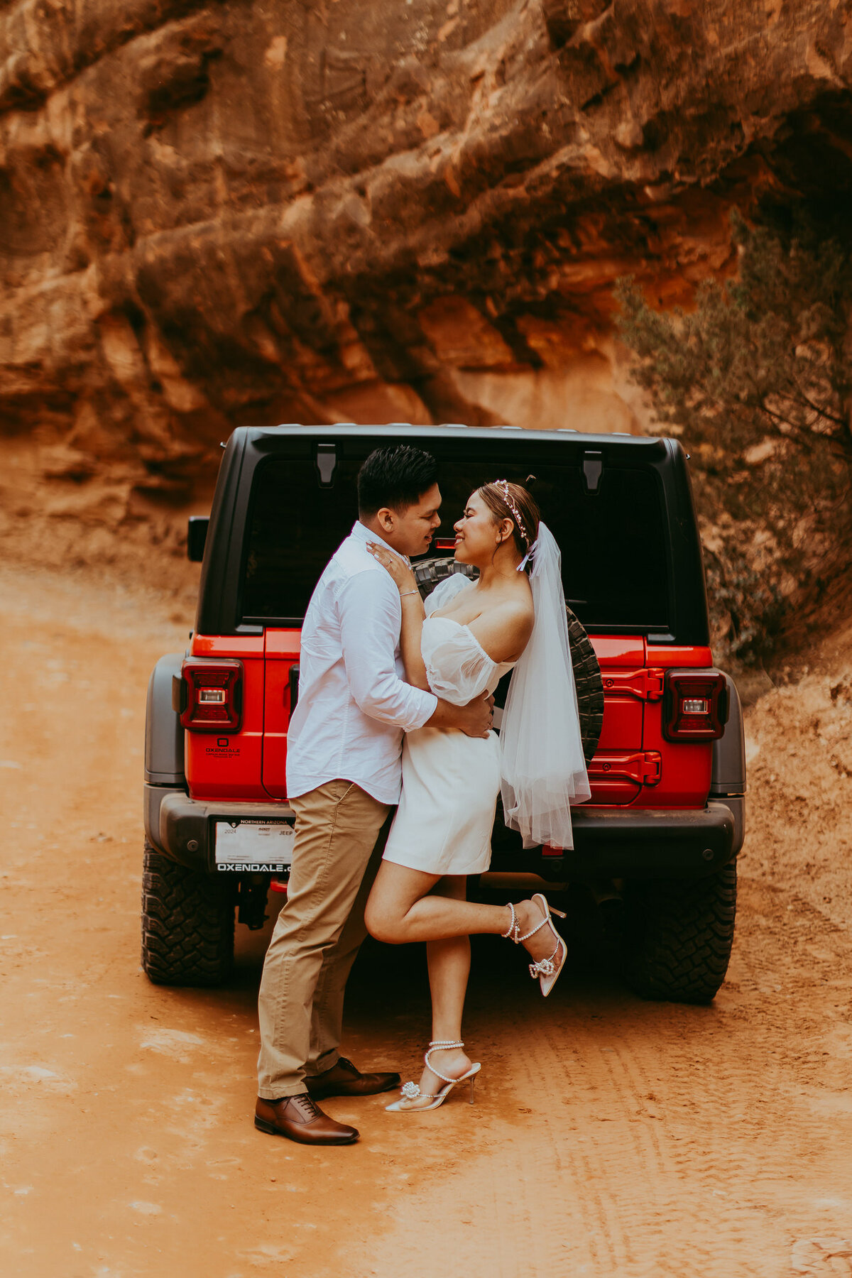 couple stands together with red jeep