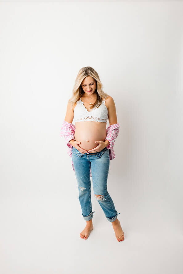 A woman expecting a baby holds her bare belly and looks at it.