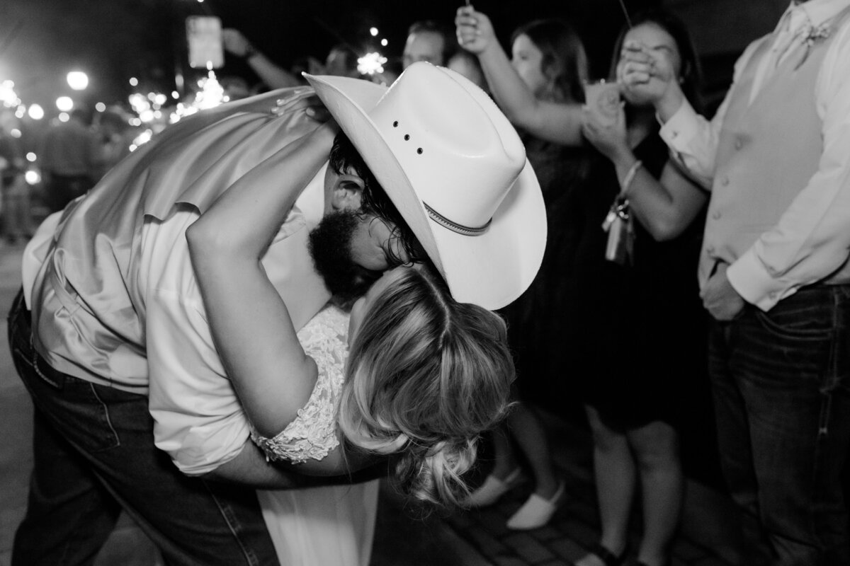 groom in a tan cowboy hat dips his bride backwards and kisses her as she wraps her arms around his neck for their grand exit
