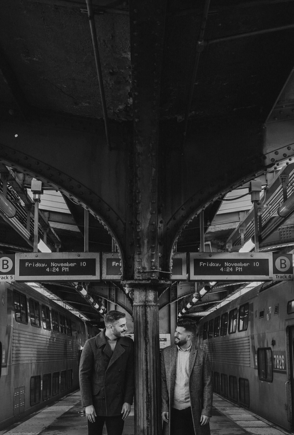 A couple standing on either side of a pillar in a train station 
