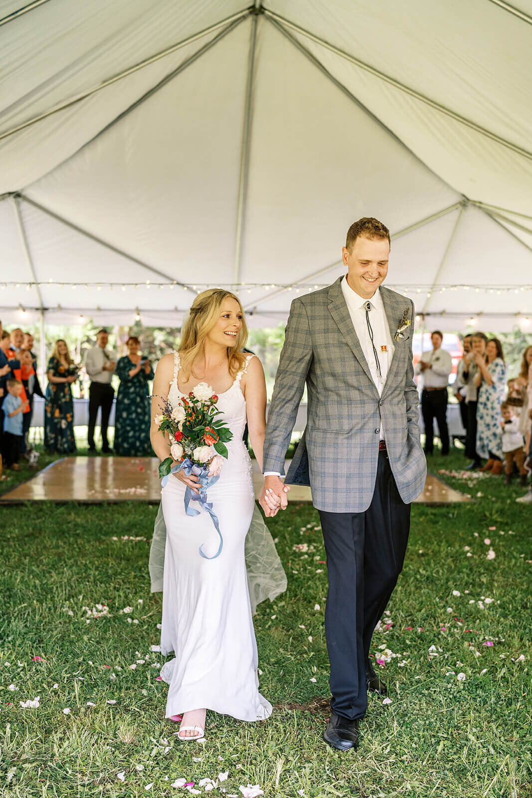 A bride and groom hold hands at an outdoor wedding reception.