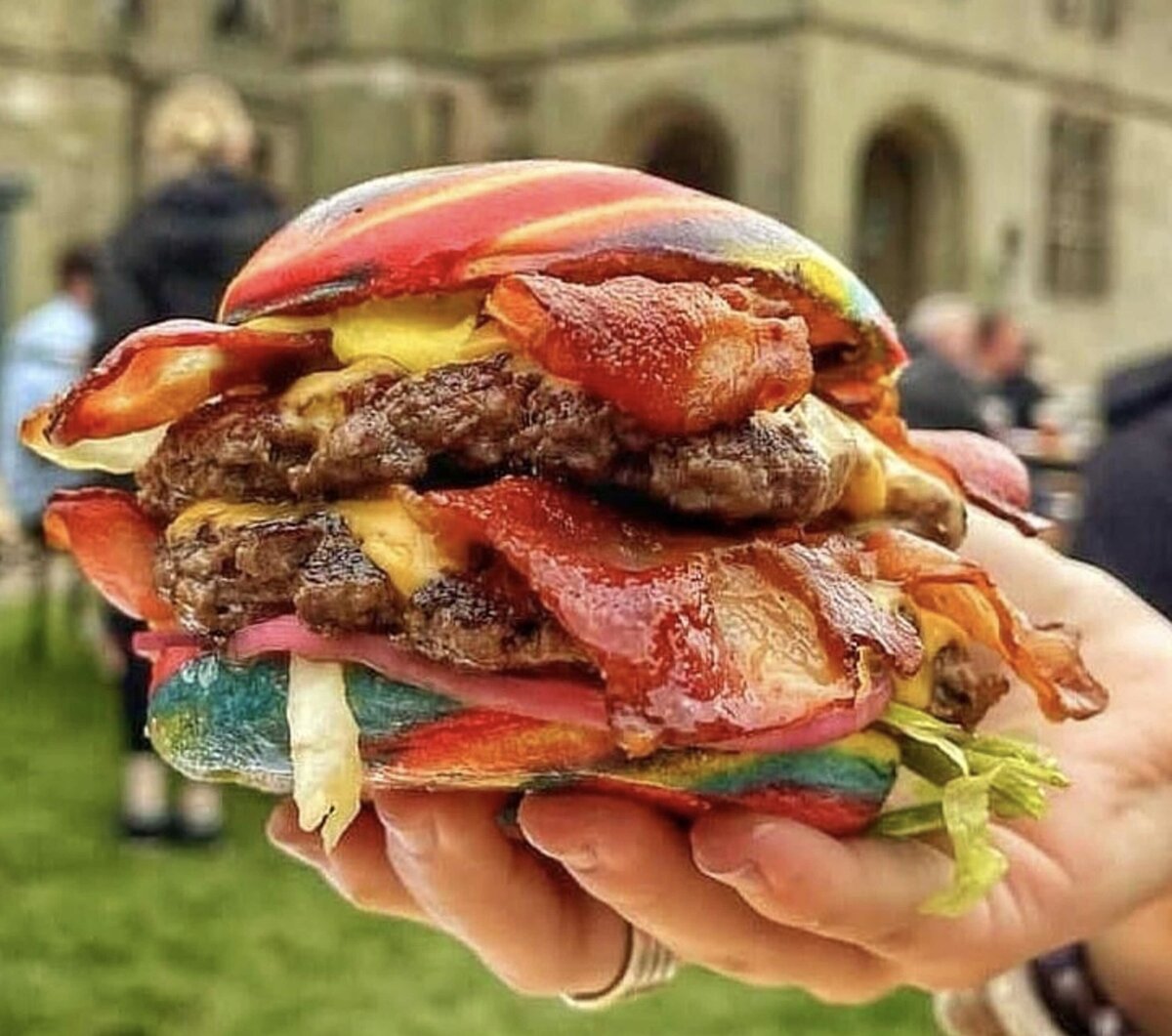 hand holding rainbow coloured bun with double beef burger patties. In front of Lichfield Cathedral