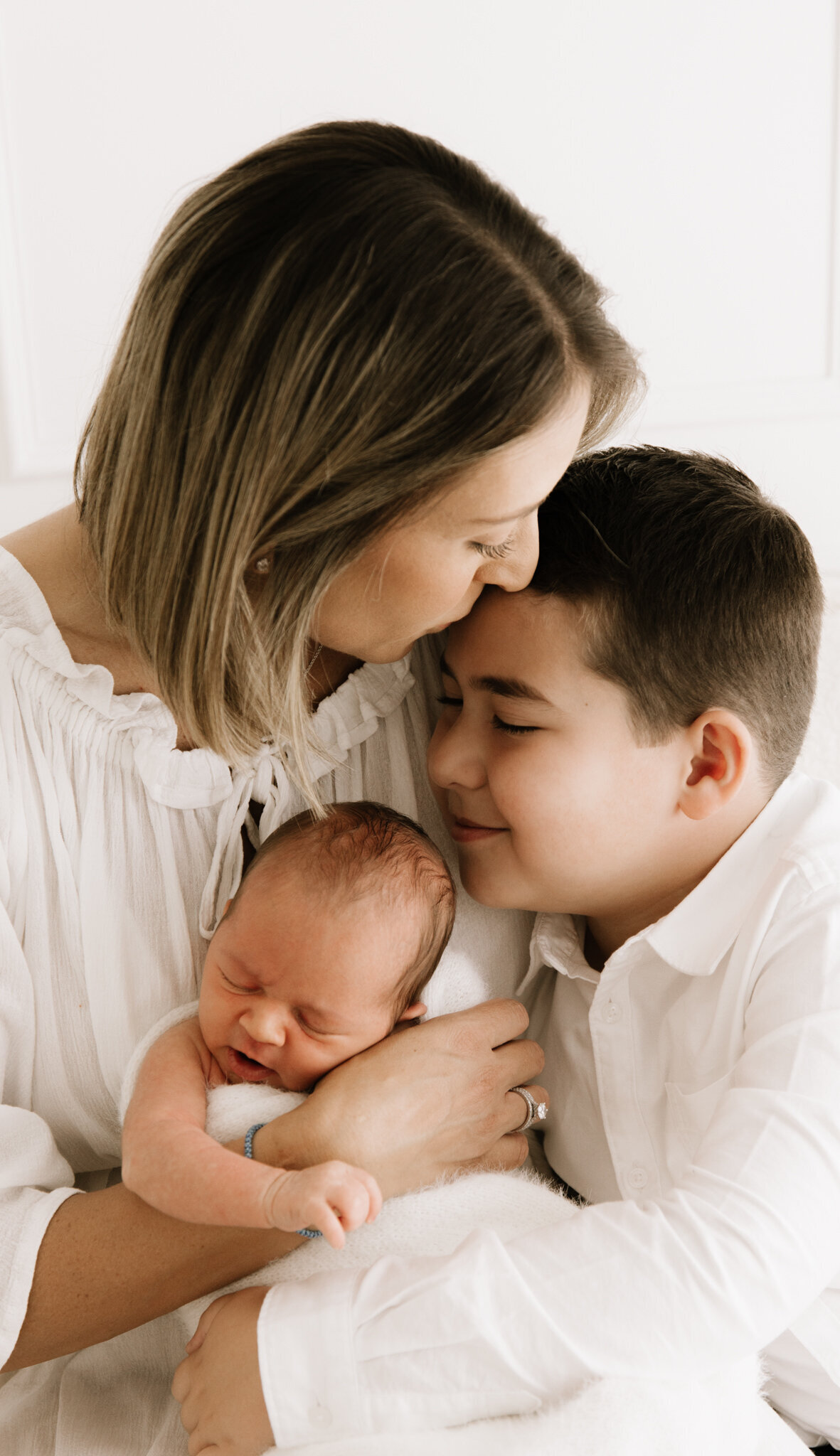 Mother embracing her newborn and older son in a tender sibling moment during a family newborn photography session in Southwest Sydney studio.