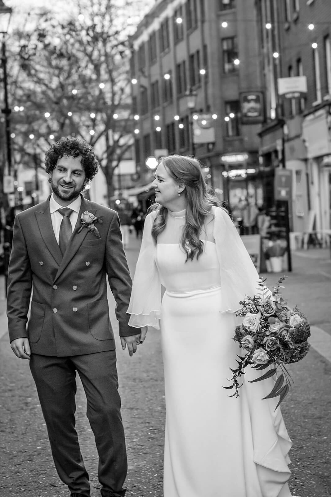 Bride smiling to groom as they walk down Exmouth market . Black and white image