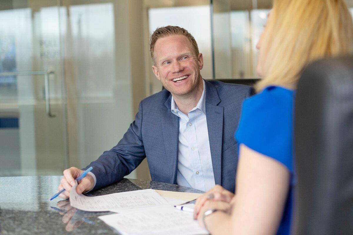 Laughing businessman in a glass conference room, meeting with a blonde woman in a blue shirt