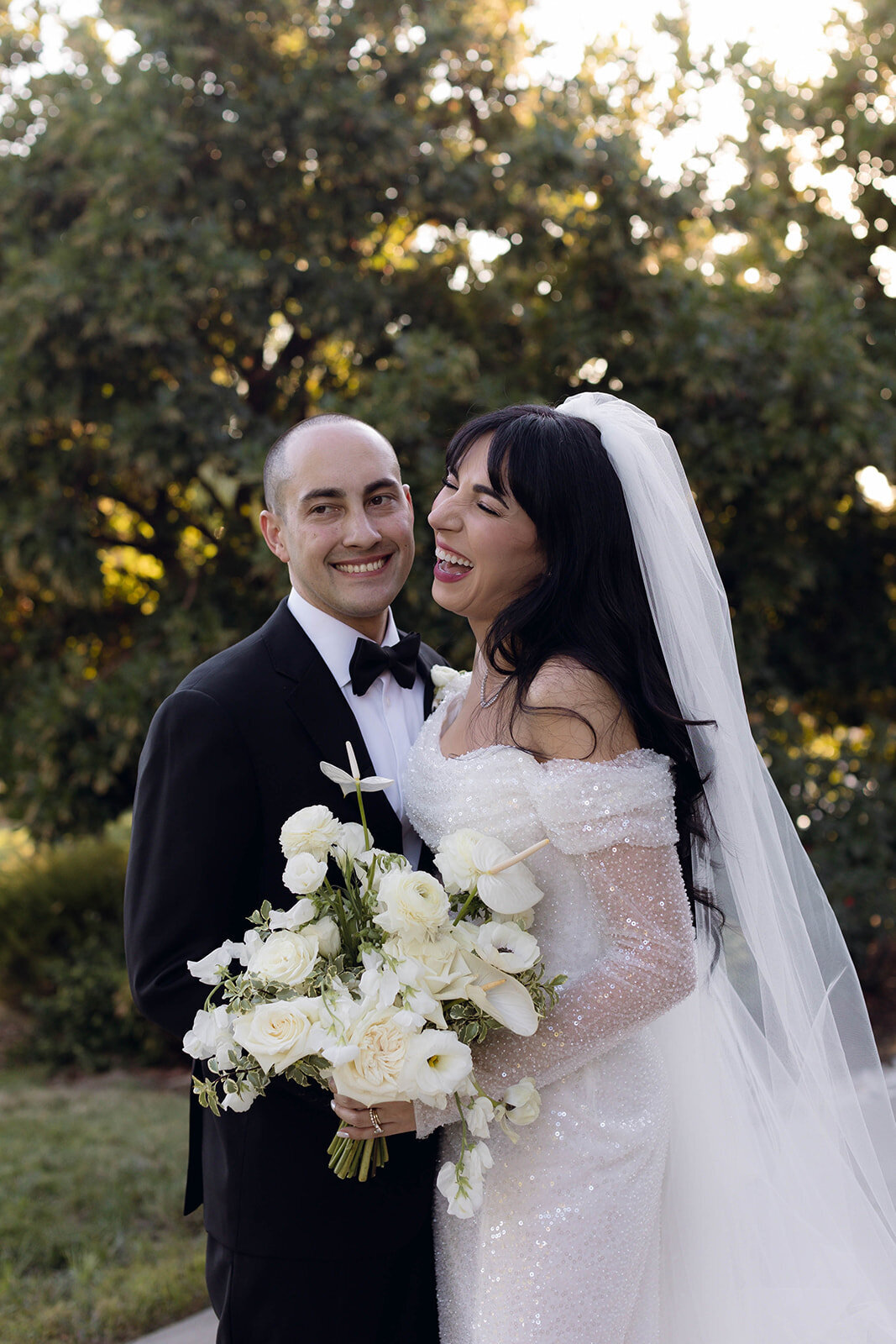 A candid moment of a newlywed couple laughing together, surrounded by golden light and nature. An editorial-style wedding photo showcasing genuine joy and connection.