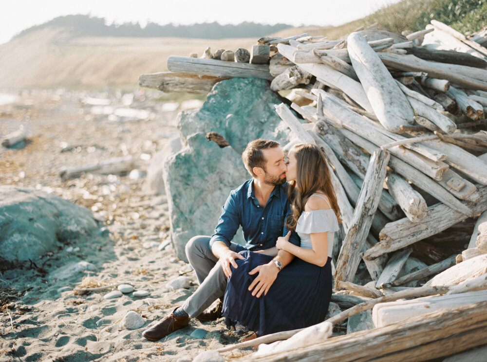 couple kissing at the beach near driftwood