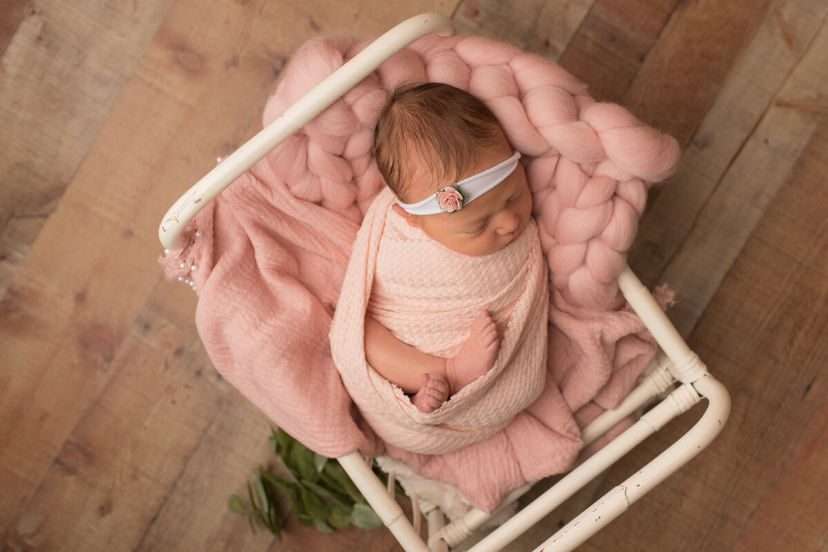 Baby girl wrapped in blush pink wrap with pink headband and white crib