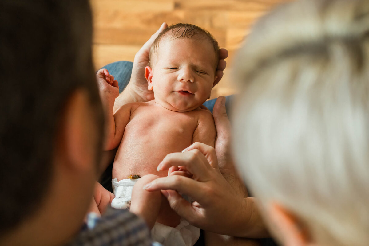 Newborn baby being held by mom and dad peeking from behind their heads