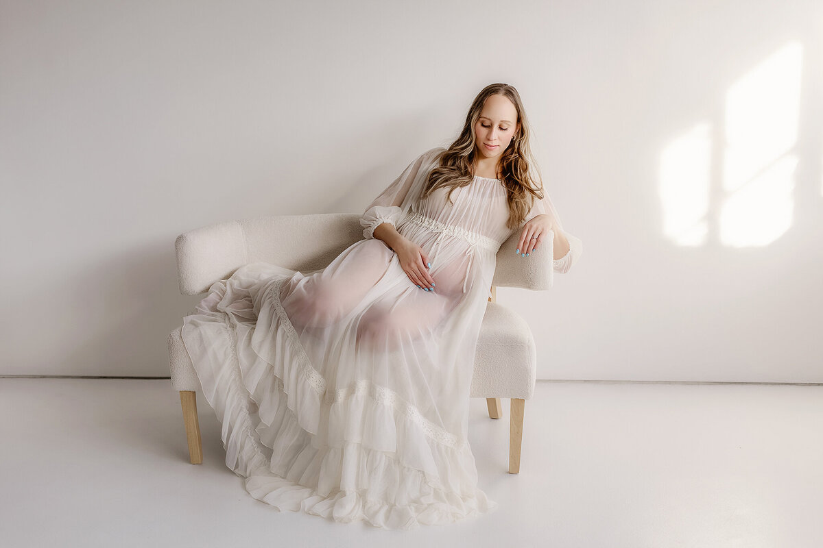 A mother drapes a sheer fabric around her belly in an ethereal maternity picture, highlighting the softness of pregnancy.