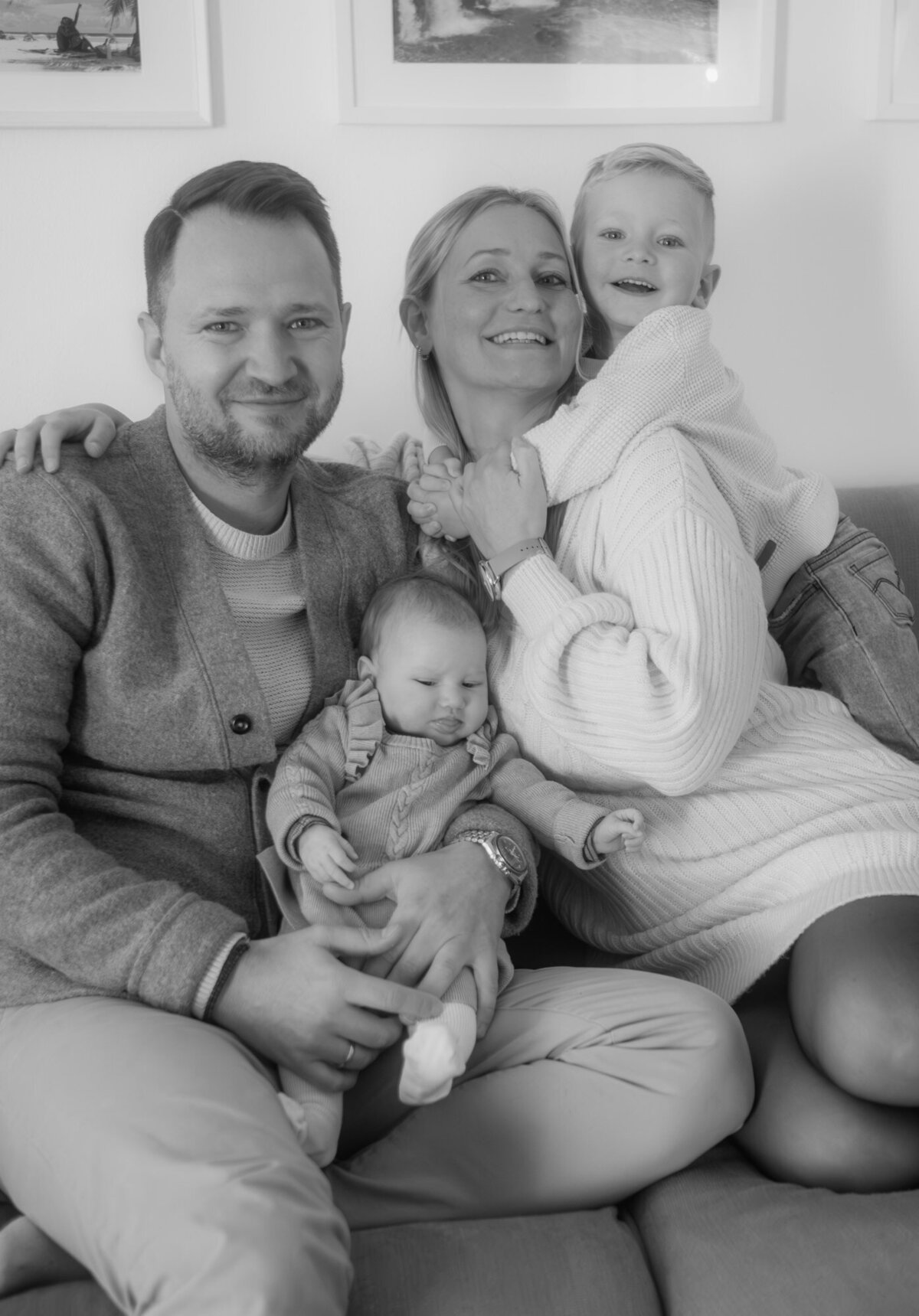 Family picture with a newborn sitting on dads lap, while the older son hugs his mom.