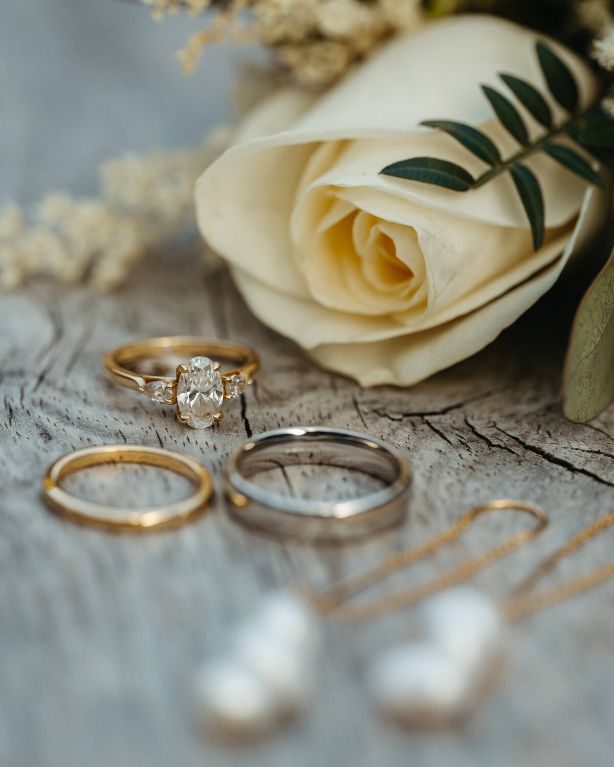 Gold and silver wedding bands with pearl earrings on wooden surface