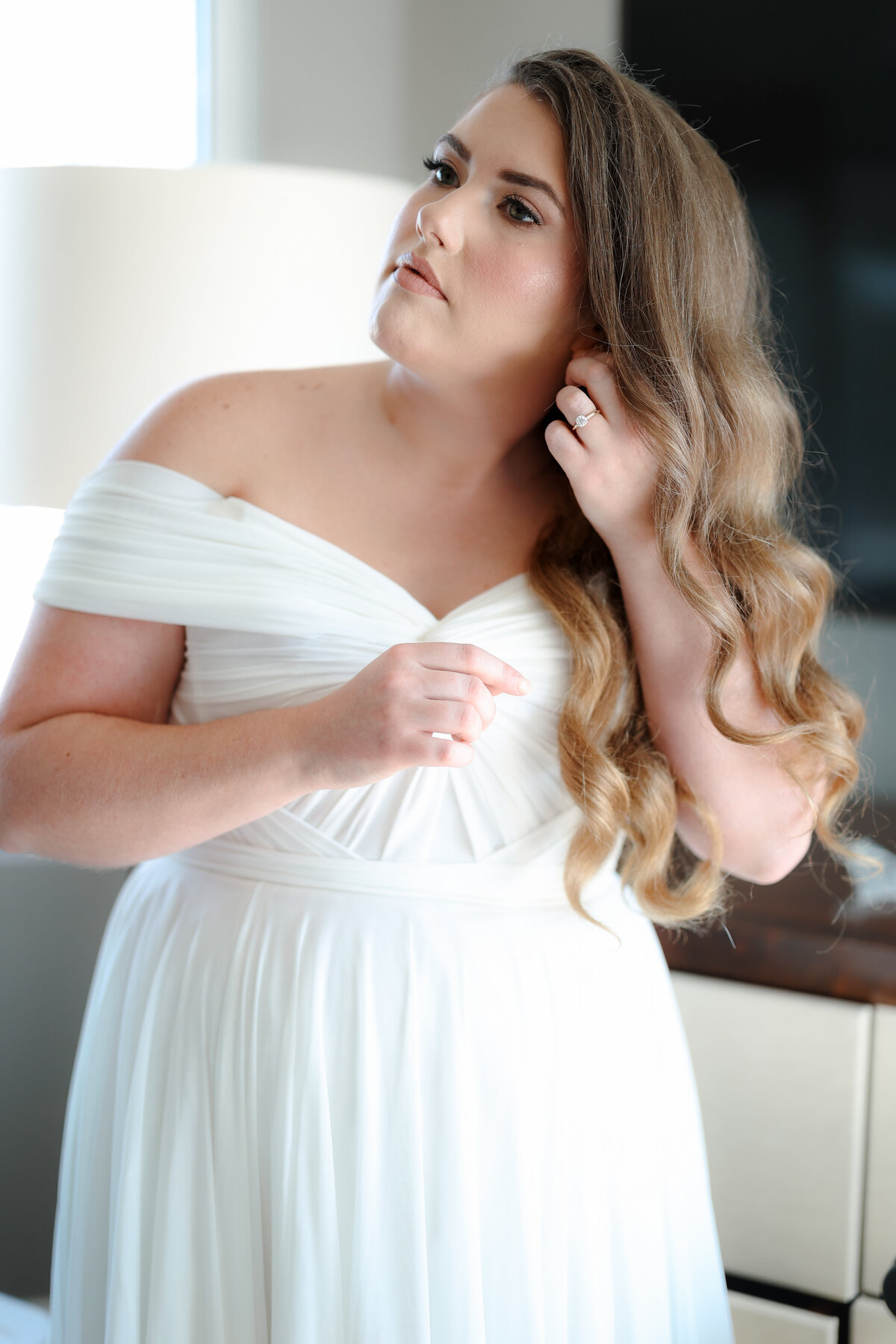 Bride preparing for her wedding day, gently adjusting her veil and dress in a peaceful, light-filled room.