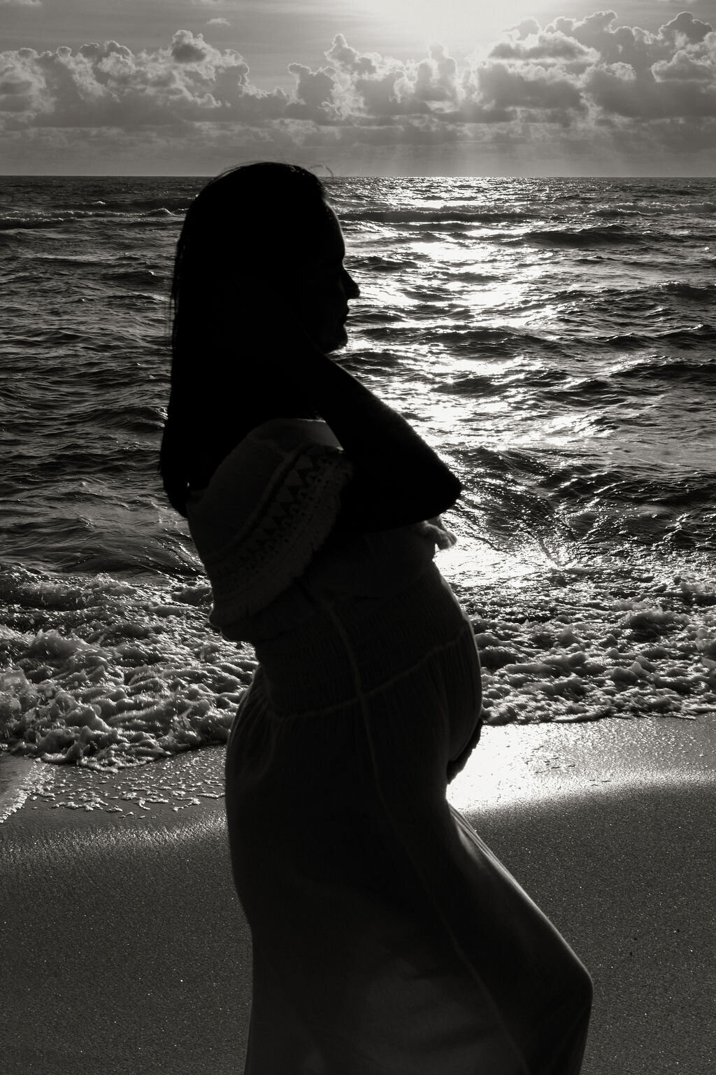 Silhouette of a pregnant woman standing at the edge of the ocean during sunrise in Sunny Isles Beach.